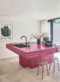 a kitchen with pink counter tops and stools next to an open floor plan window