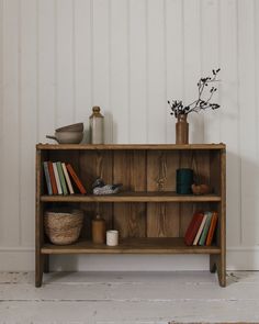 an old wooden shelf with books and vases on it, against a white wall