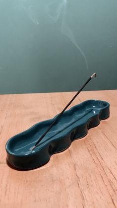 a blue ceramic incense bowl with two black sticks sticking out of the top, on a wooden table