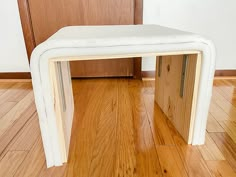 a white bench sitting on top of a hard wood floor next to a wooden door