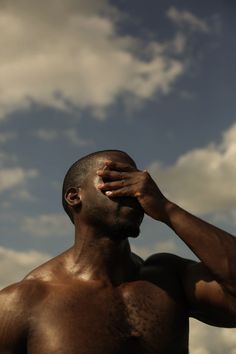 a shirtless man is holding his hand to his face while looking up into the sky