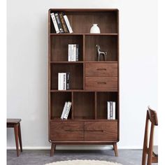 a wooden bookcase with many books on top of it next to a chair and table