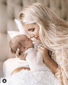 a woman holding a baby in her arms and kissing it's face with both hands