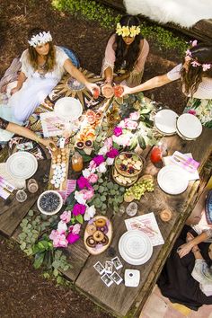 people sitting at a picnic table with plates and flowers in their hair, holding hands