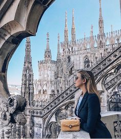 a woman standing on top of a stone wall next to a building with spires