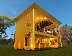 a yellow building that is lit up with lights on the outside and inside, in front of some trees