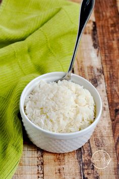 a white bowl filled with rice on top of a wooden table next to a green towel