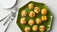 a green plate topped with mini crab cakes next to a fork and knife on a white table