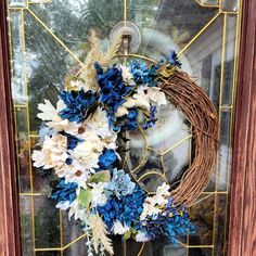 a wreath with blue and white flowers is on the front door glass window sill