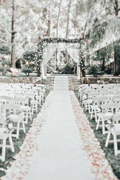 an outdoor ceremony setup with white chairs and greenery on the aisle, surrounded by trees