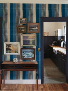 a hallway with blue and white striped wallpaper, wooden flooring and artwork on the walls