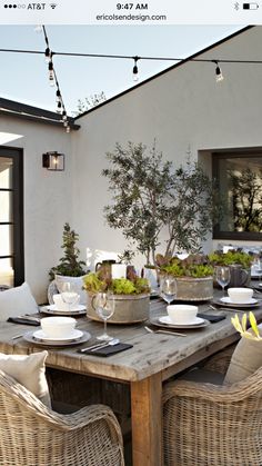 an outdoor dining area with wicker chairs and wooden table set for four, surrounded by potted trees