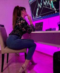 a woman sitting in front of a computer monitor on top of a desk with a purple light