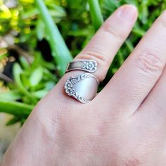 a woman's hand with a silver ring on top of it and green plants in the background