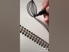 a hand holding a black wire next to an egg beater on top of a piece of paper