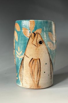 a ceramic cup with an image of a bird on it's side and leaves in the background