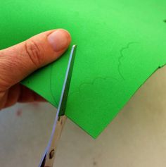 someone cutting out a piece of green paper with scissors