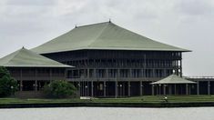 a large building sitting on top of a lake next to a lush green forest covered hillside