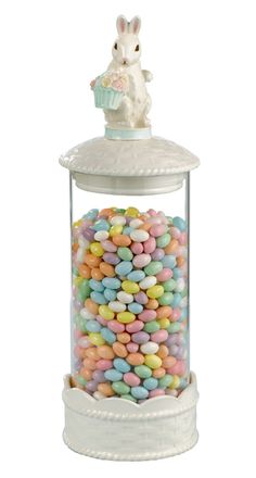 a glass jar filled with lots of colorful candy next to a white rabbit figurine