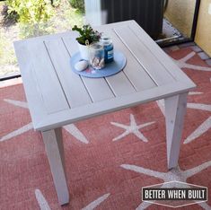 a white table with a blue plate on it sitting in front of a window next to a potted plant