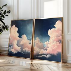 two framed pictures with clouds on them in front of a potted plant and window