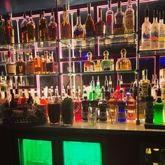 many bottles and glasses are lined up on the wall behind a bar with neon lights