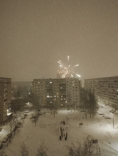 fireworks are lit up in the night sky over snow covered ground and buildings with lights on them