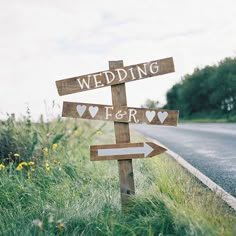 a wooden sign with hearts on it sitting in the middle of a grass field next to a road