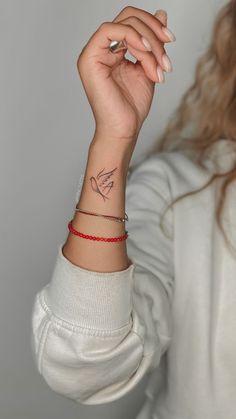 a woman wearing a red string bracelet with a small tattoo on her arm and wrist