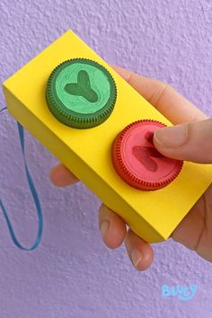 a hand holding a yellow box with two green and red buttons on the top,