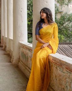 a woman in a yellow sari sitting on the side of a building with columns