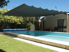 an empty swimming pool in front of a house with a sun shade over the pool