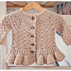 a crocheted sweater with ruffled sleeves and buttons is hanging on a wooden hanger