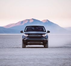 the front end of a black land rover driving on a desert plain with mountains in the background