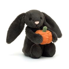 a black stuffed rabbit holding a pumpkin