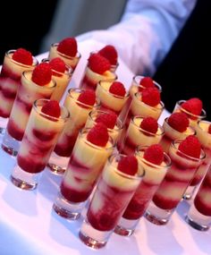 small desserts are lined up on a white tray with raspberries in them