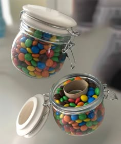 two glass jars filled with colorful candy on top of a white table next to each other