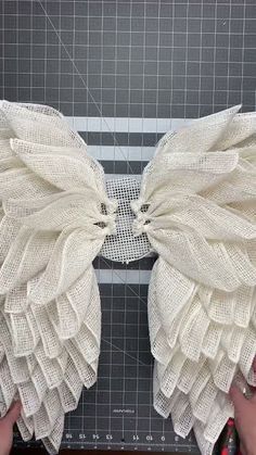 two hands are working on an object made out of yarn and fabric with white wings