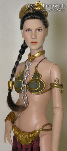 a doll wearing a gold and red outfit with chains on it's neck, in front of a white wall