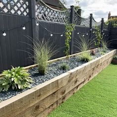 a long wooden planter filled with plants next to a fence and grass covered yard