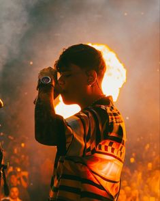 a man standing in front of a fire with his hand up to his face while holding a microphone