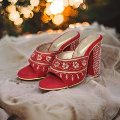 a pair of red high heeled shoes sitting on top of a white cloth covered bed