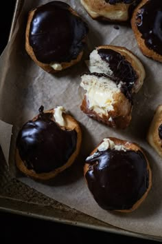 chocolate covered doughnuts sitting on top of a piece of wax paper in a box