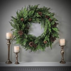 a wreath with pine cones and candles on a mantle