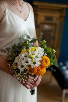 a woman in a white dress holding a bouquet of yellow and white flowers on her wedding day