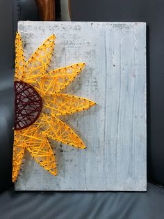 a string art sunburst sitting on top of a gray couch next to a vase