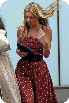 a woman in a polka dot dress walking down the street with her hair blowing in the wind