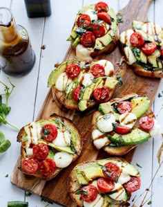 several open faced sandwiches with tomatoes, avocado and mozzarella on a wooden cutting board