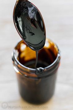 a glass jar filled with liquid sitting on top of a wooden table next to a spoon