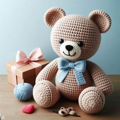 a crocheted teddy bear sitting next to a gift box and yarn balls on a table